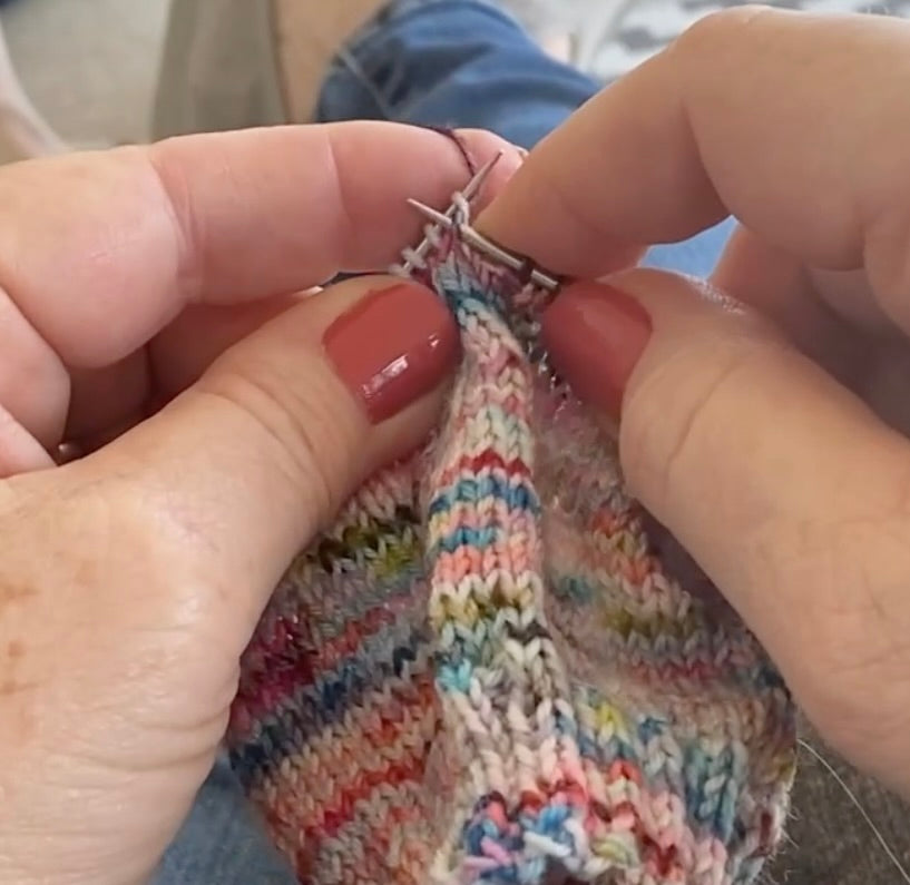 hands holding knitting needles and yarn as they are knitting a sock